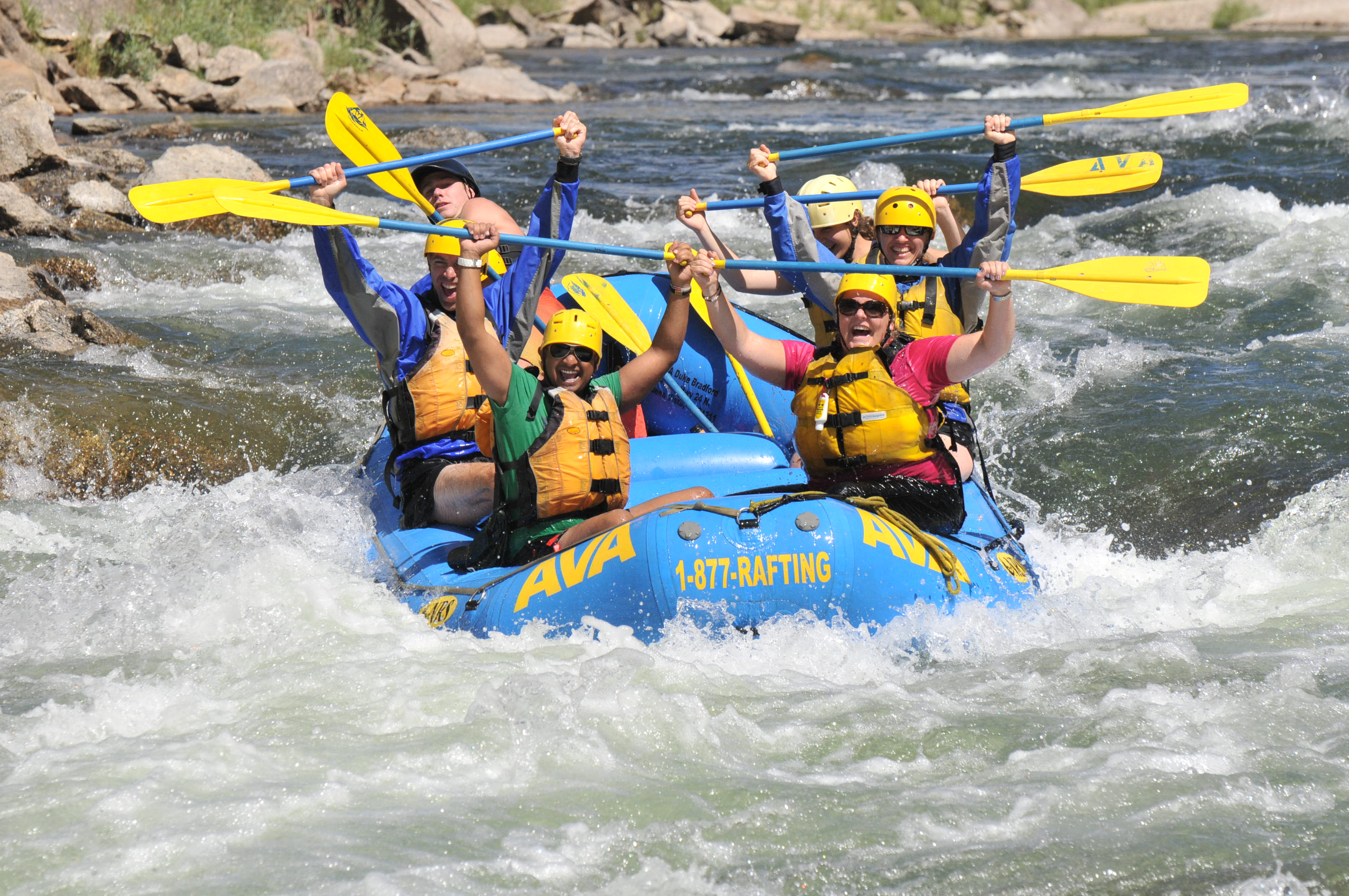 A group of six rafters with their paddles up while rafting the river