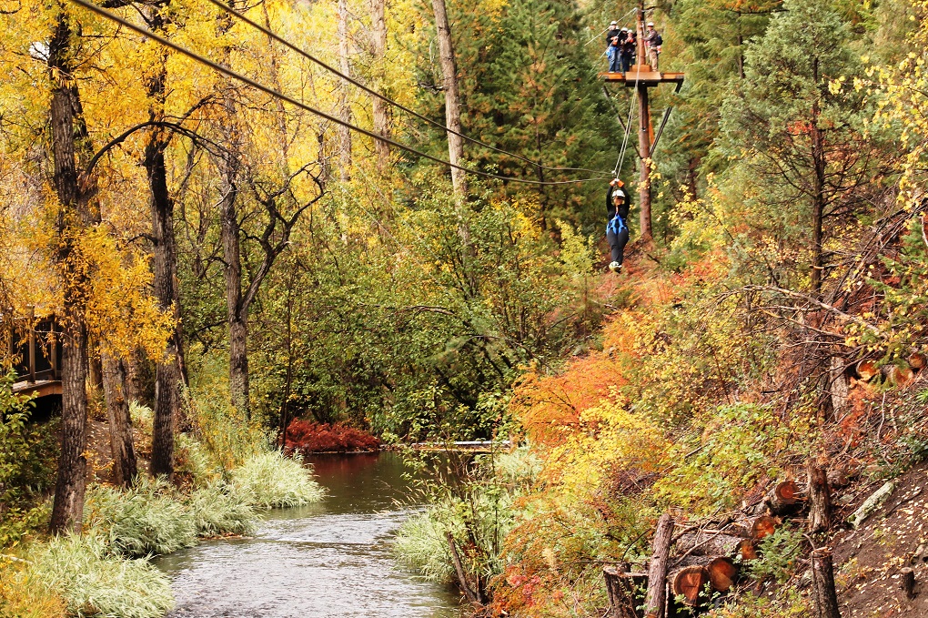 woman ziplining over a river with orange, yellow and green fall foliage everywhere