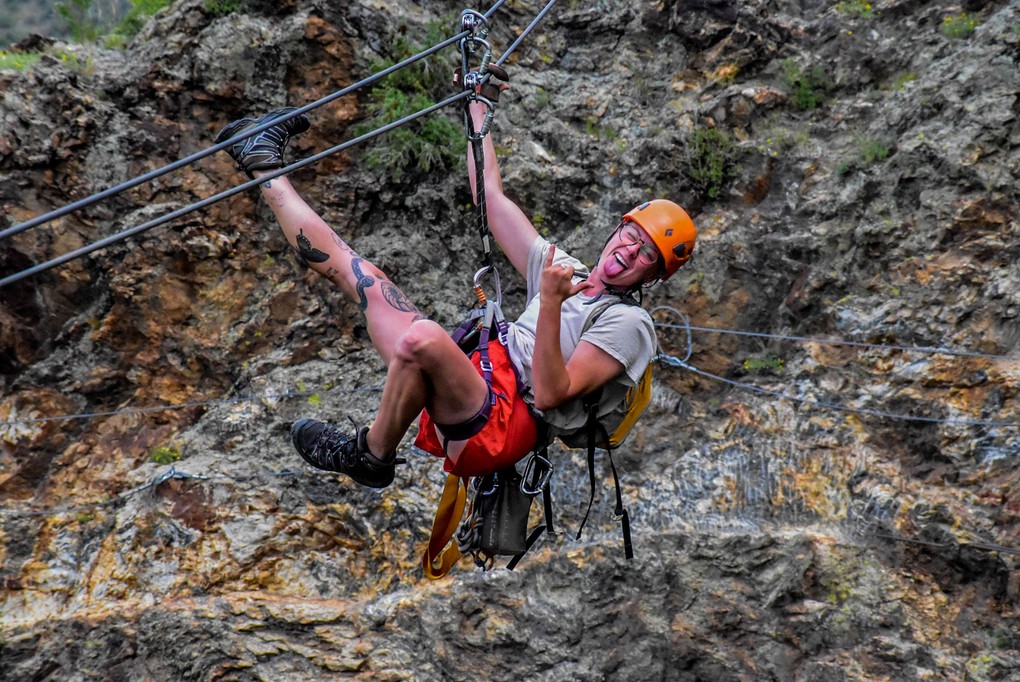 A person mid zipline with their leg up and a hang loose sign