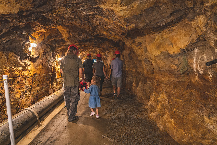 People walk down a corridor in the Argo Mine in Idaho Springs wearing red hard hats 