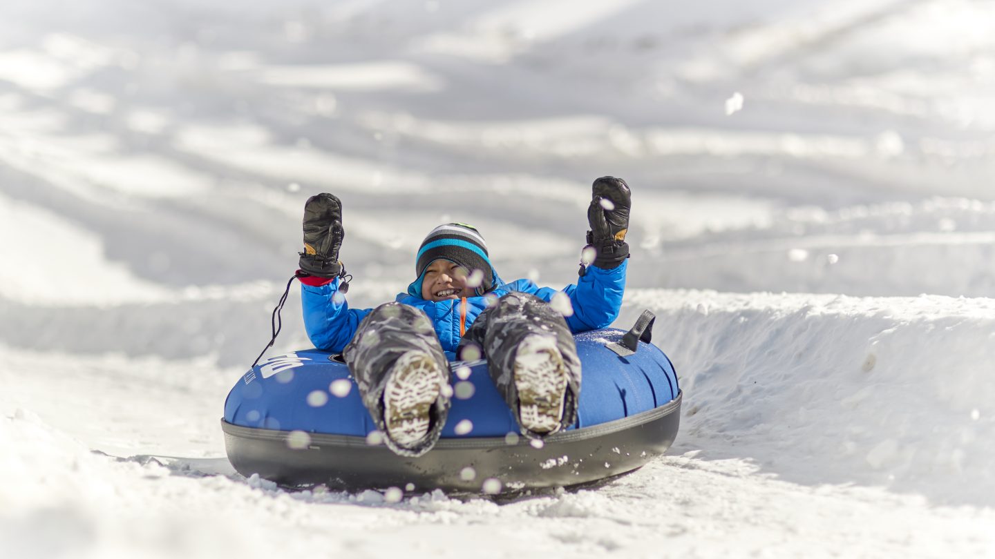 A child snow tubing down echo mountain with his hands raised