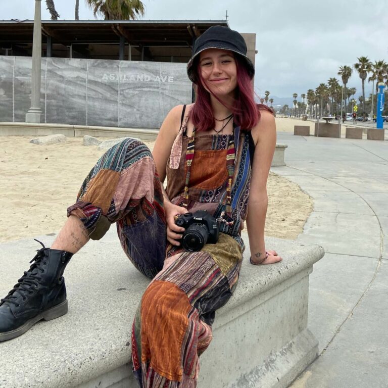 Woman with a canon camera on her lap sitting on a cement bench by the beach